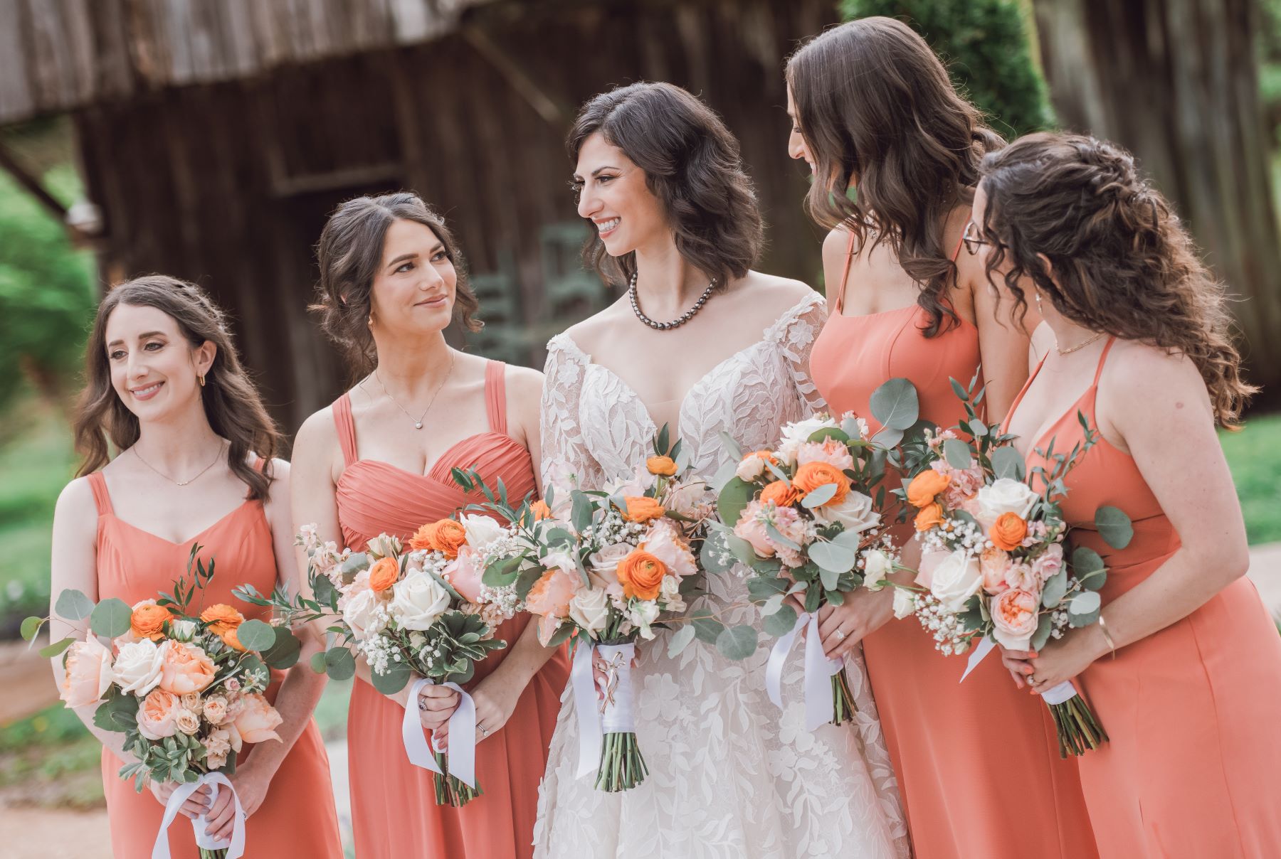 smiling bridesmaids are outside and holding flowers
